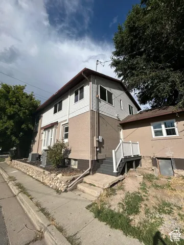 Exterior featuring a two-story brick and siding facade, stone retaining wall, and raised entrance deck with white railings