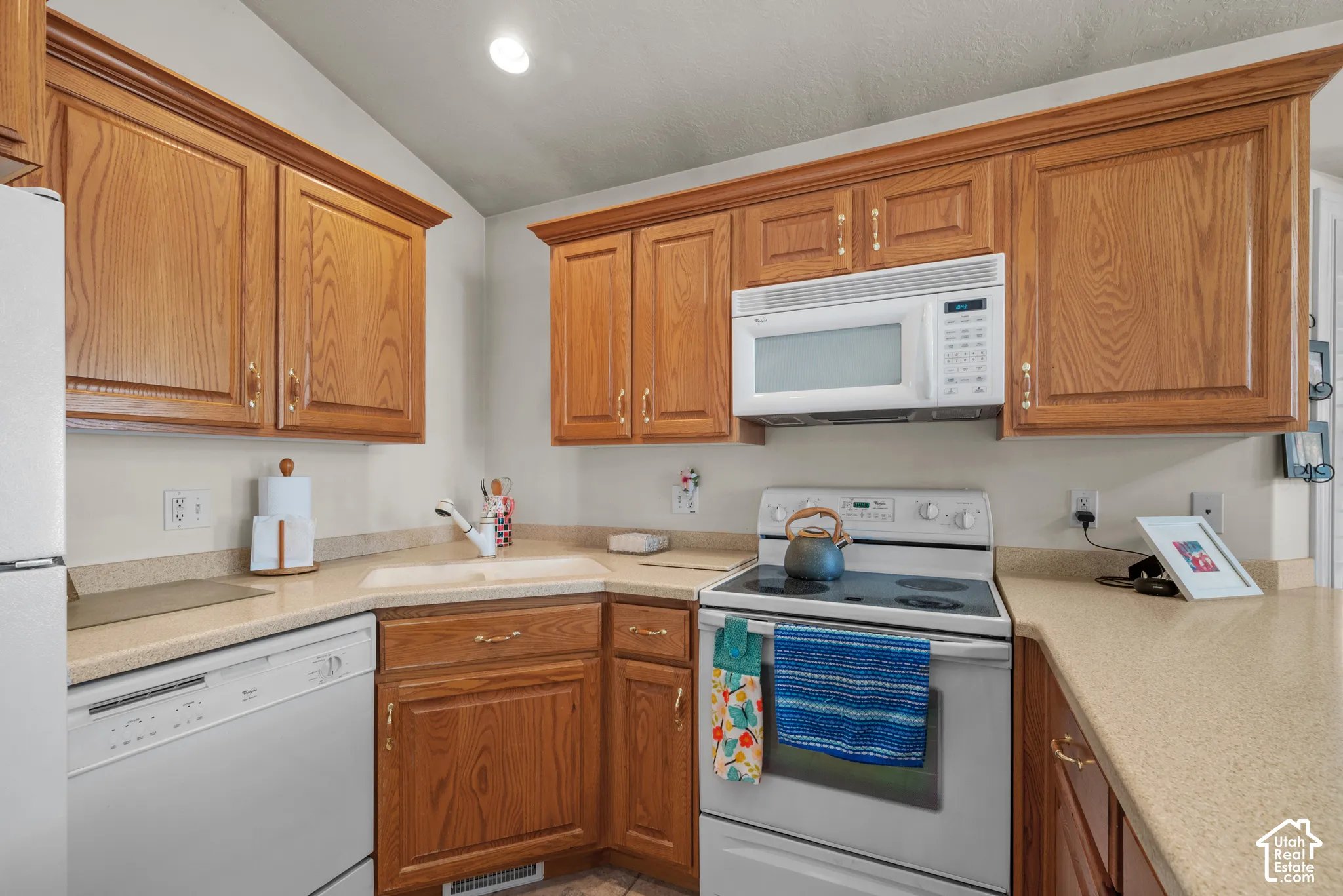 Kitchen featuring honey-tone cabinetry, solid-surface countertops, recessed lighting, and white appliances including a dishwasher, built-in microwave, and electric range