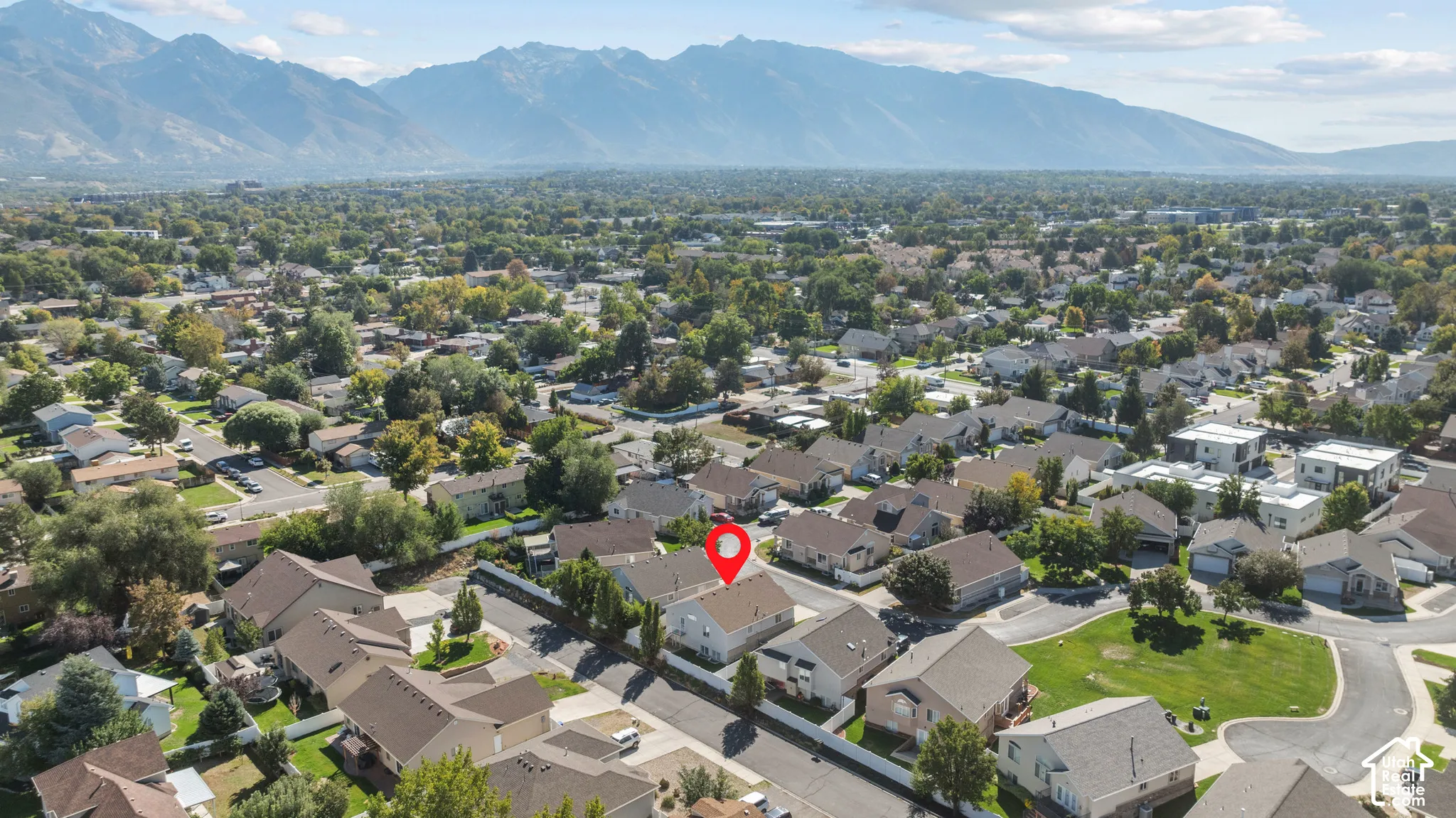 Aerial perspective featuring a residential lot with a paved driveway and mature perimeter landscaping, set against a prominent mountain backdrop