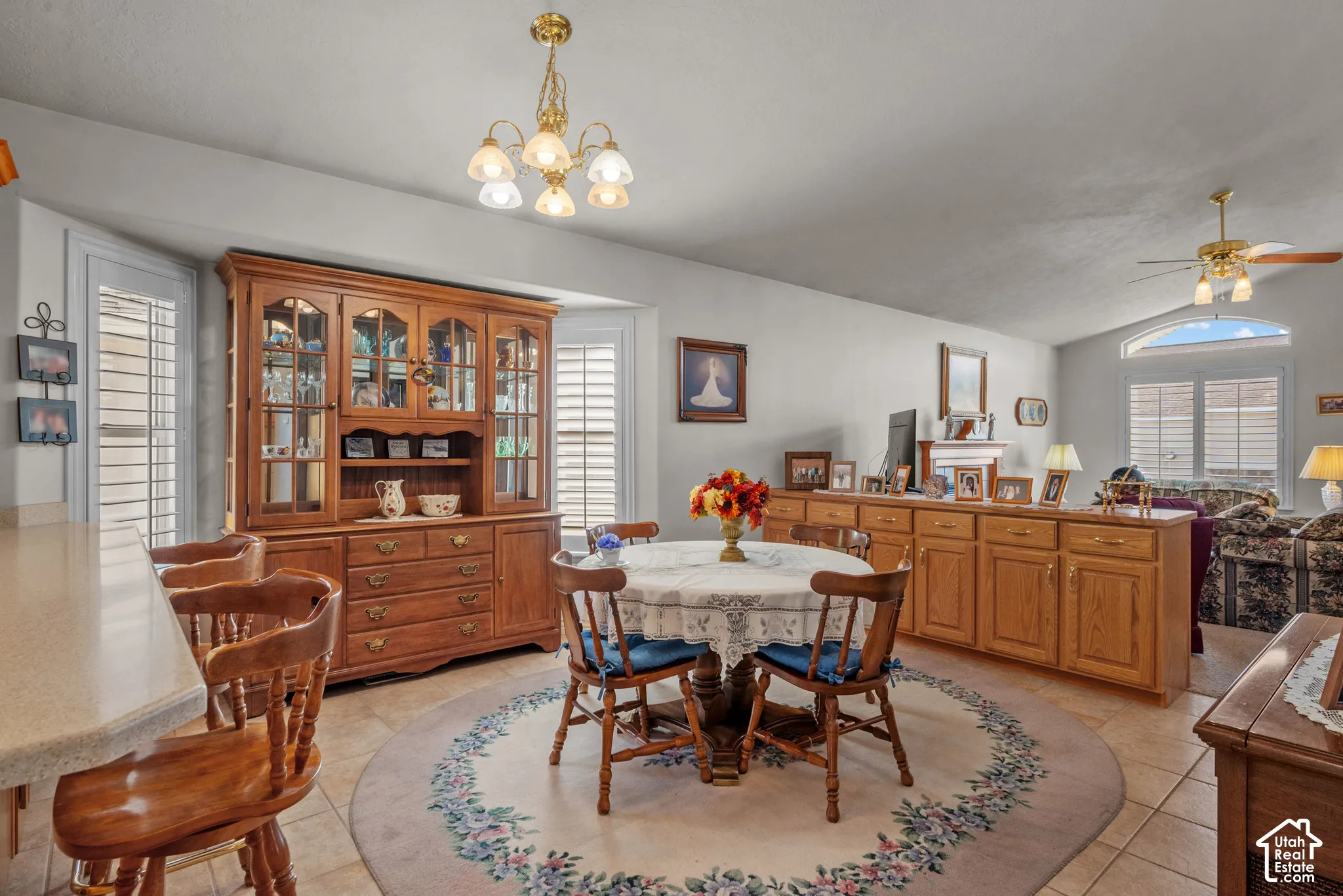 Dining area featuring tile flooring, built-in wooden cabinetry, plantation shutters, a multi-light chandelier, and vaulted ceilings
