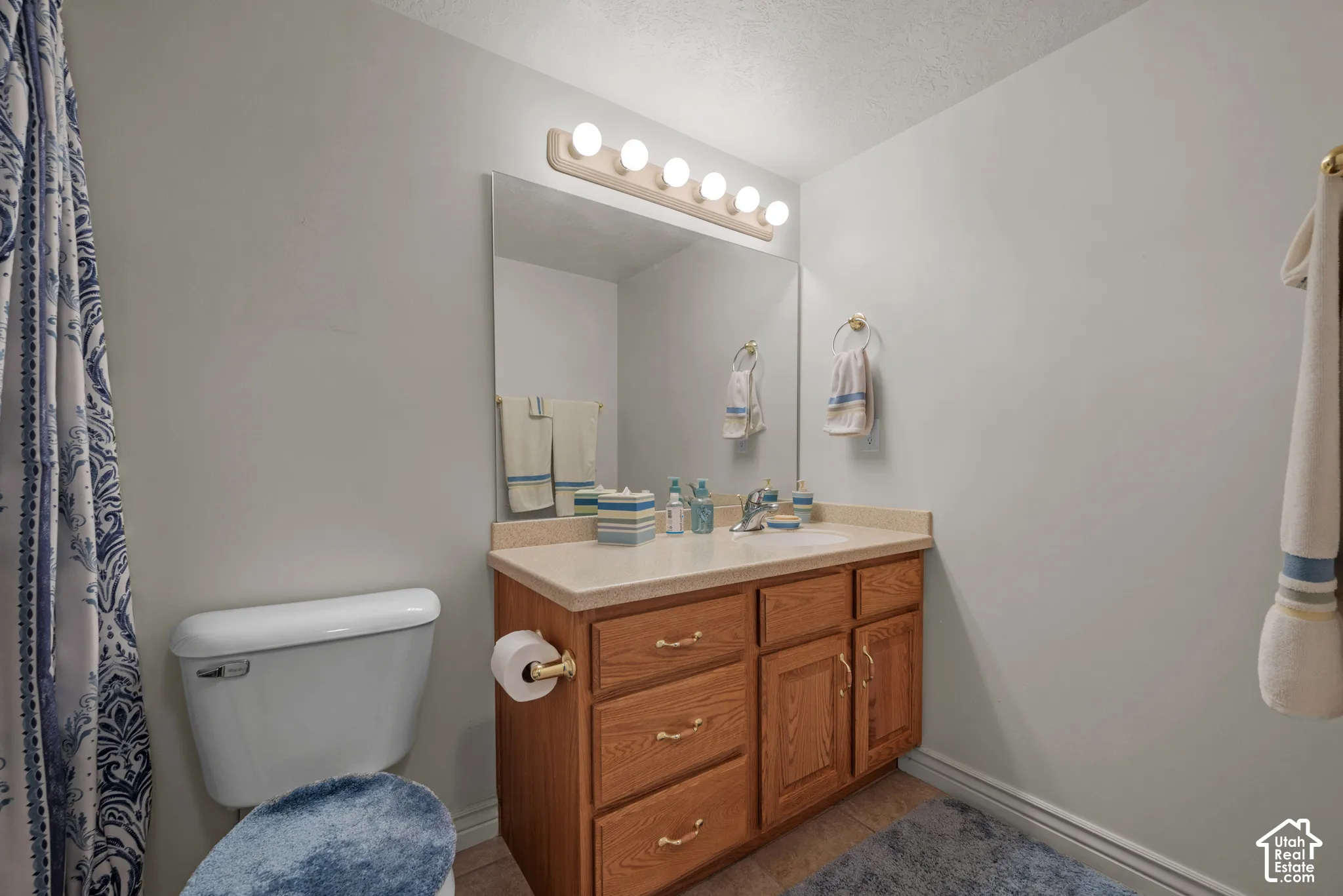 Bathroom vanity featuring medium-tone wood cabinetry, a solid surface countertop with integrated basin, polished brass hardware, and a five-bulb wall-mounted light fixture above a large plate glass mirror