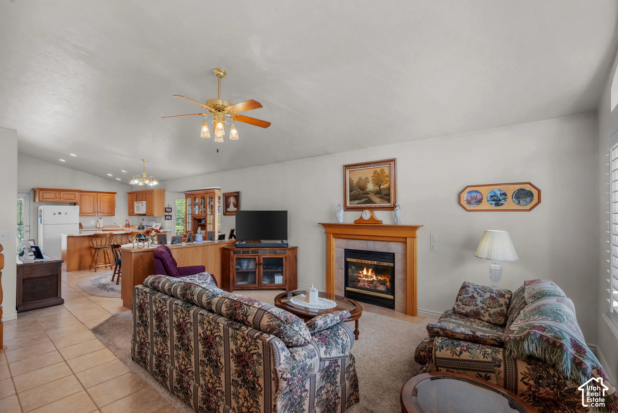 Vaulted ceilings, tiled flooring, fireplace with a wood mantle, ceiling fan with integrated lighting, and wooden cabinetry