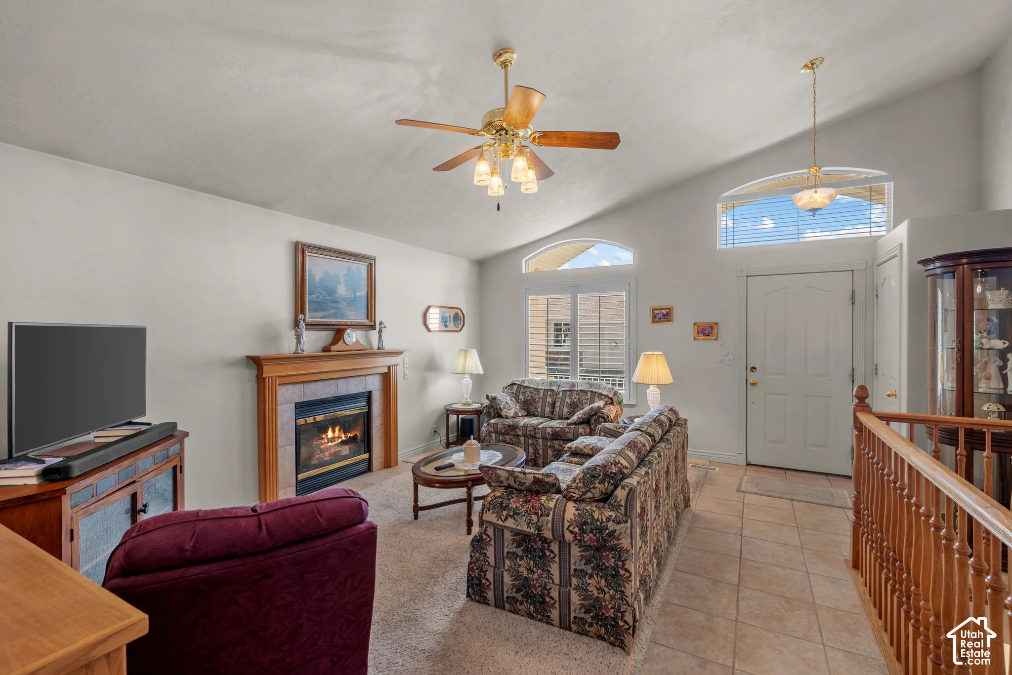 Vaulted ceilings featuring a built-in fireplace with a tile surround and wood mantel, arched windows, and wood-finish railing