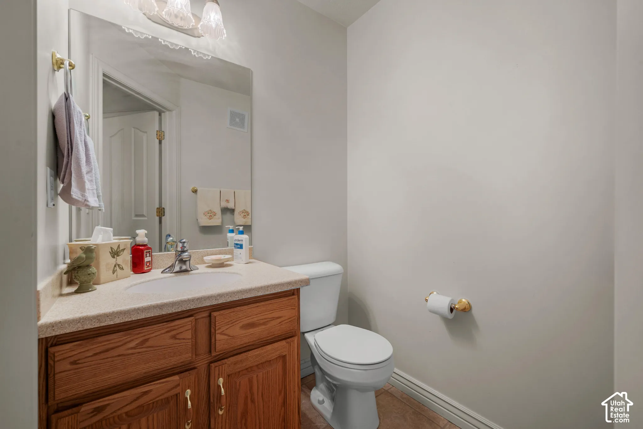 Bathroom featuring a vanity with wood-finish cabinetry, integrated solid-surface countertop with an oval basin, wall-mounted mirror, three-light fixture, and brass-tone hardware