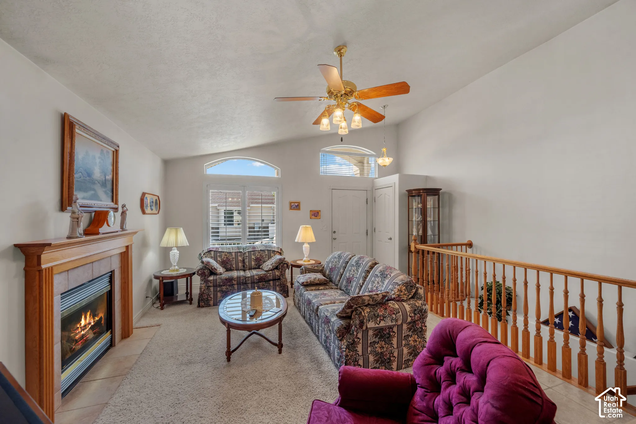 Vaulted ceilings, a fireplace with a wood mantel and tile surround, an arched window, and a wooden balustrade