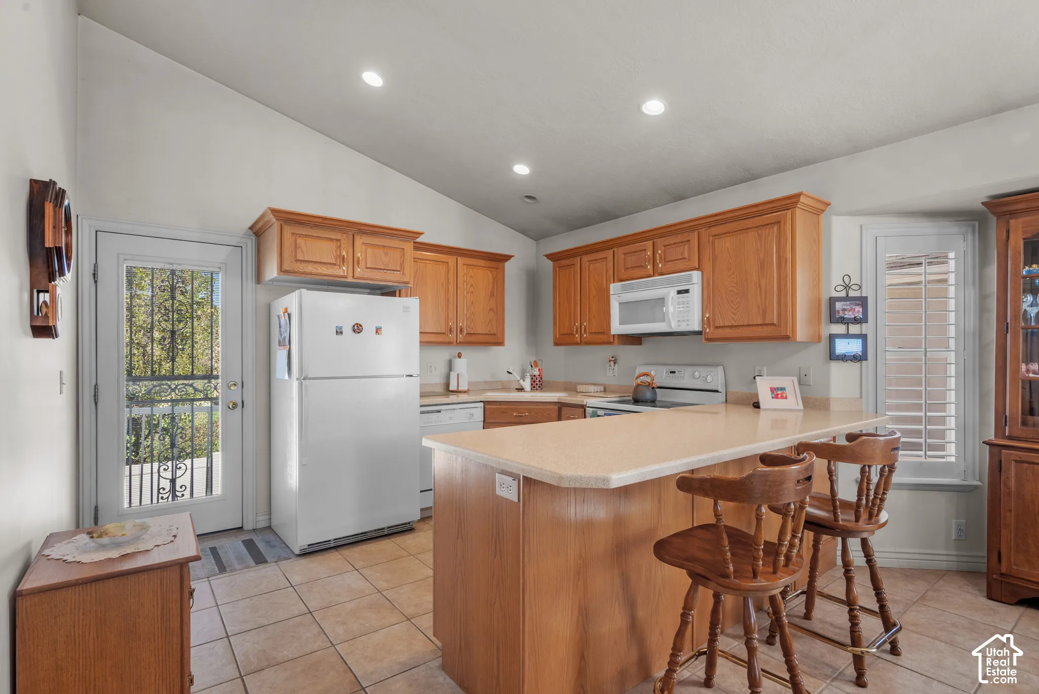 Kitchen featuring vaulted ceilings, wood-finish cabinetry, a peninsula countertop, ceramic tile flooring, and recessed lighting