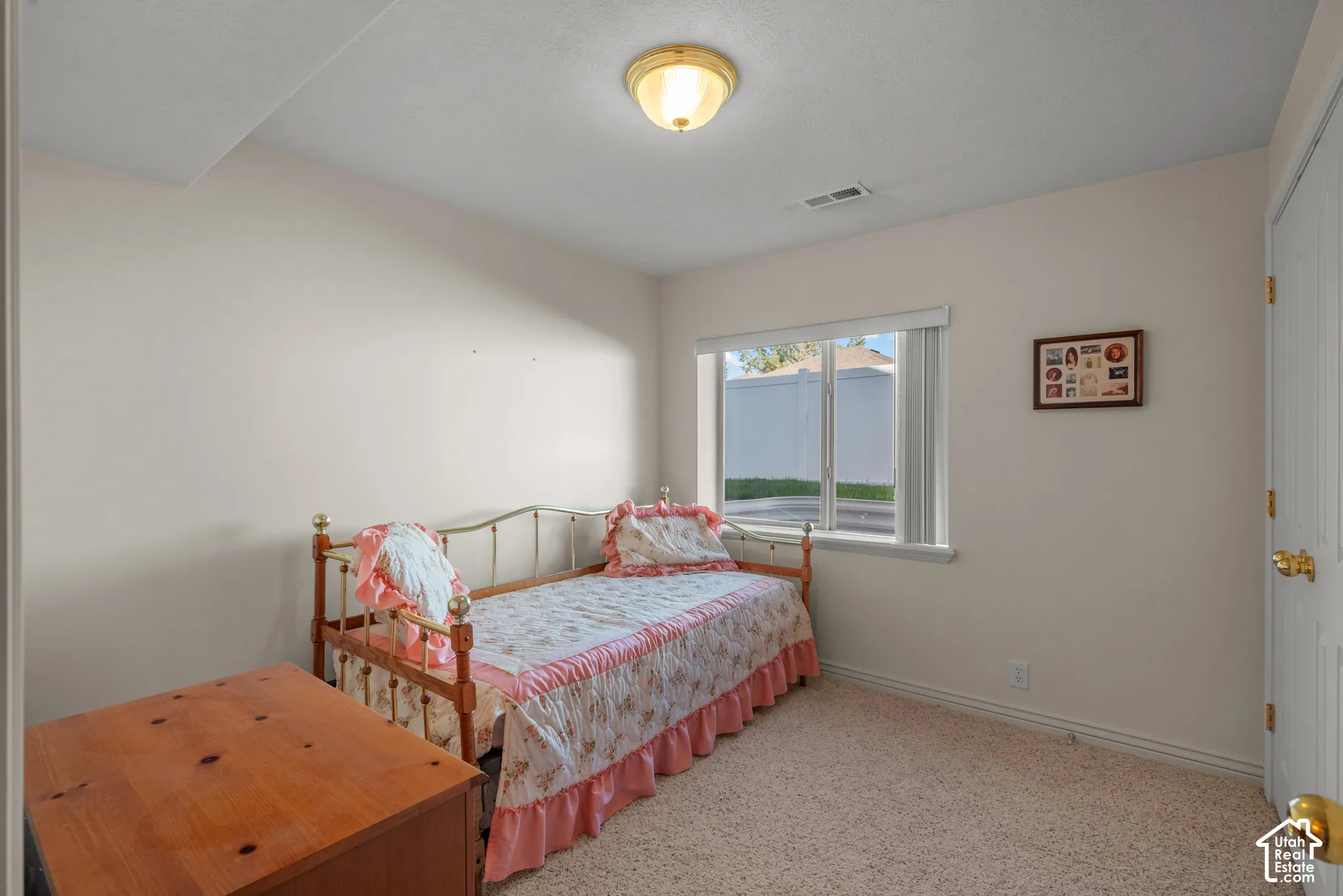 Neutral-toned bedroom featuring beige carpeting, a single-pane window with vertical blinds, and a semi-flush mount ceiling light fixture