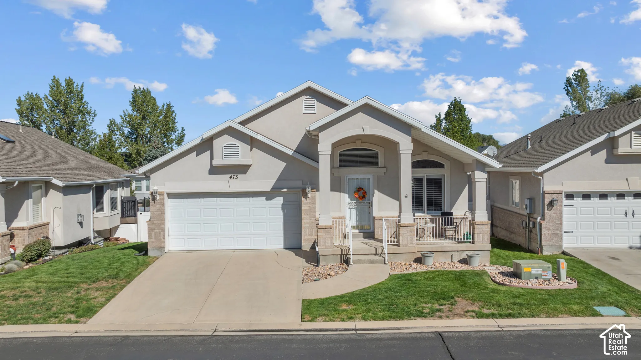 Single-story residence featuring a covered front porch with stone column bases, stucco exterior, an attached two-car garage, and a concrete driveway