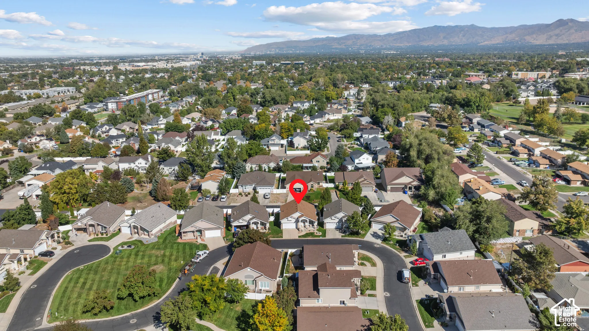 Aerial perspective featuring a single-family residence with a multi-gabled roofline and an attached garage, situated in a residential neighborhood with mountain backdrops