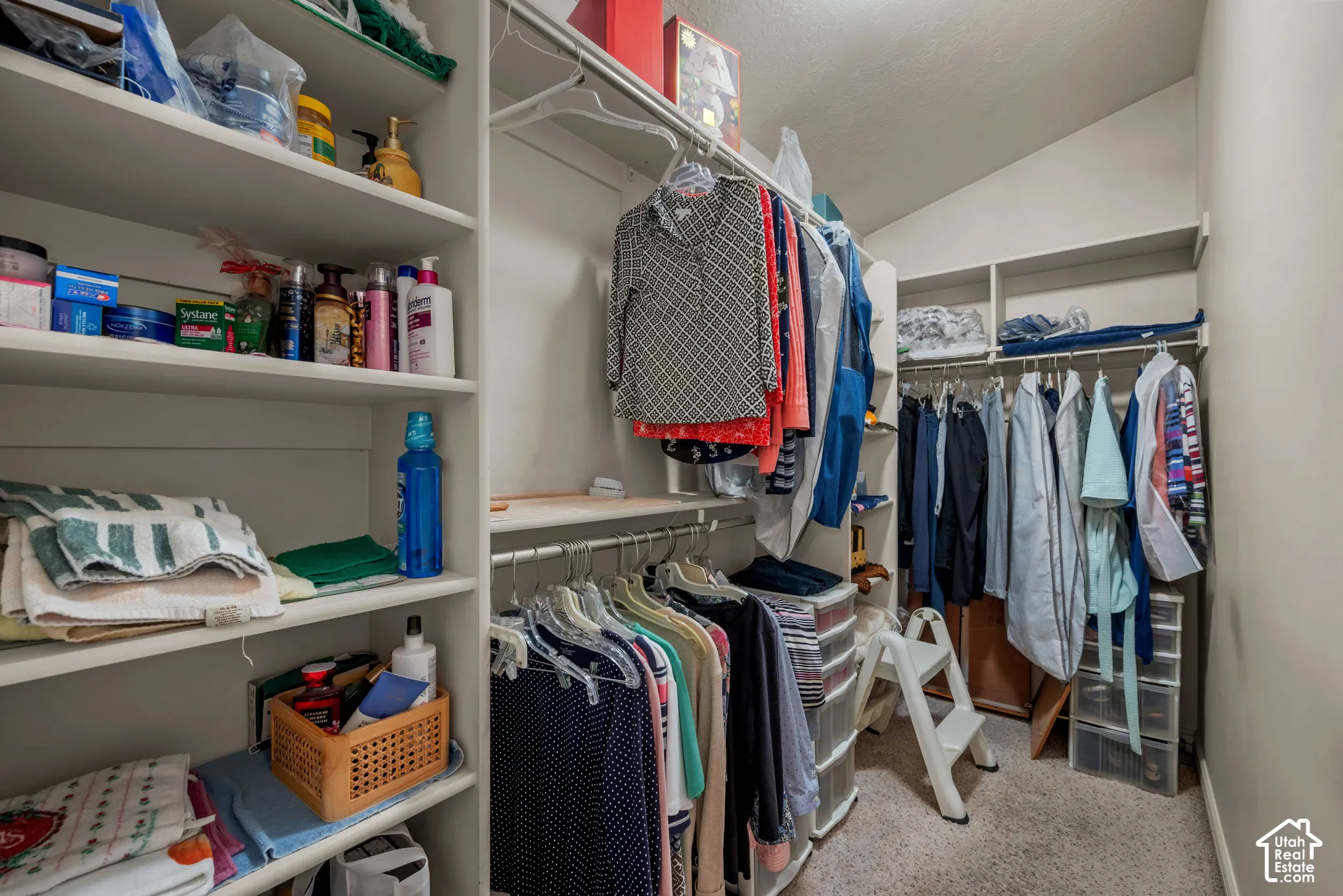 Walk-in storage space featuring built-in white shelving and tiered hanging rods