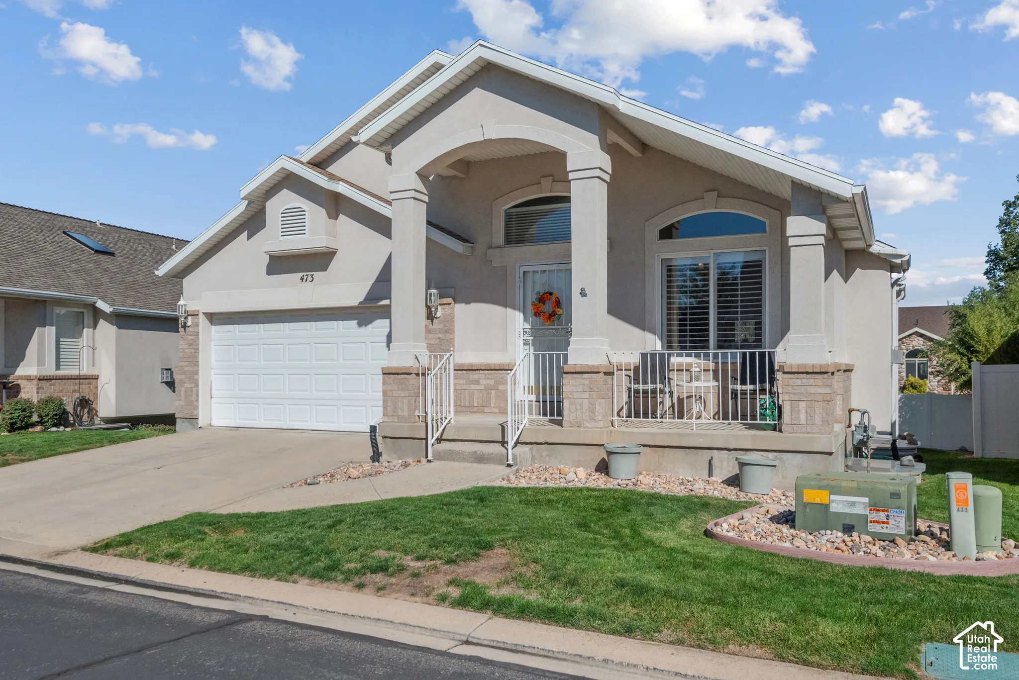 Stucco and stone exterior featuring an arched entryway, decorative columns, gabled rooflines, and a paved driveway