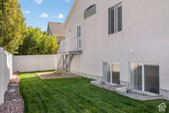 Backyard featuring a manicured lawn, white vinyl fencing, a metal staircase with a landing, and window wells