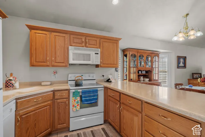Kitchen featuring wood cabinetry, integrated countertops, a built-in microwave, an electric range, and a multi-light chandelier
