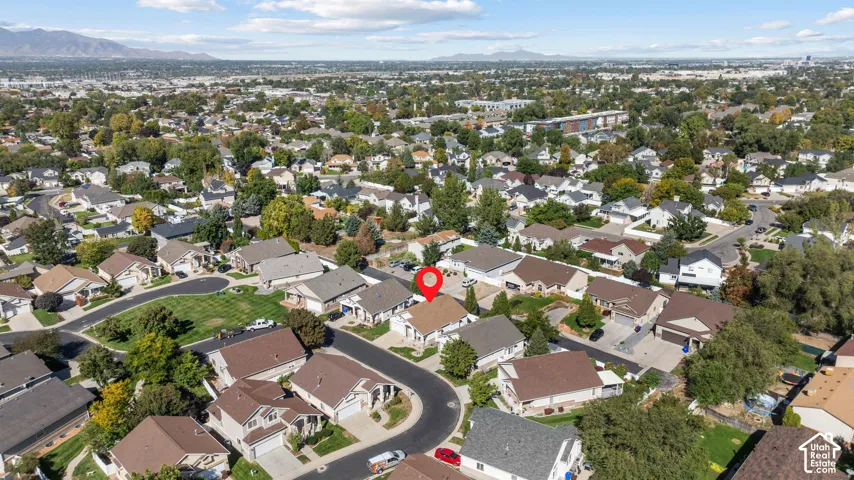 Aerial perspective of a single-story residence situated within a suburban residential community featuring paved streets, mature trees, and a mountain backdrop