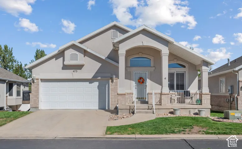 Stucco and masonry exterior featuring a covered front porch, gabled roofline, arched window detailing, and an attached two-car garage