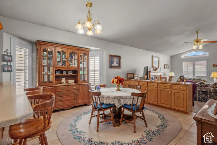Dining area featuring tile flooring, built-in wooden cabinetry, plantation shutters, a multi-light chandelier, and vaulted ceilings