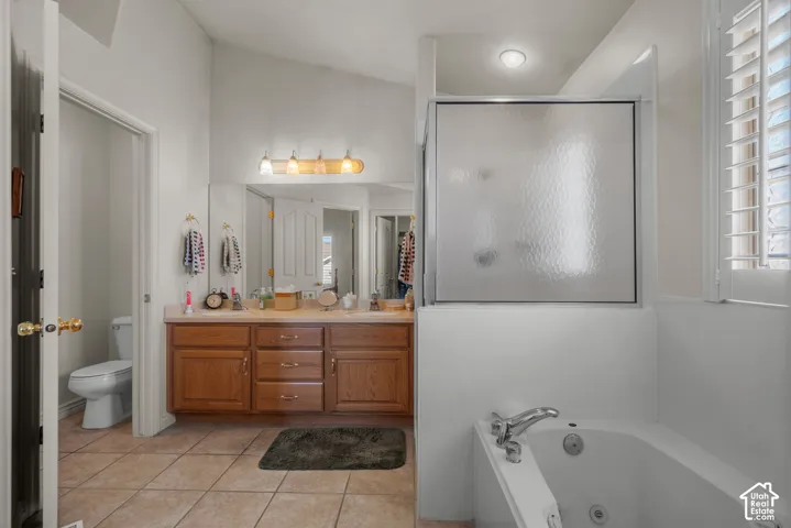 Bathroom featuring dual-sink vanity with wood cabinetry, tile flooring, built-in jetted tub, and a separate glass-enclosed shower