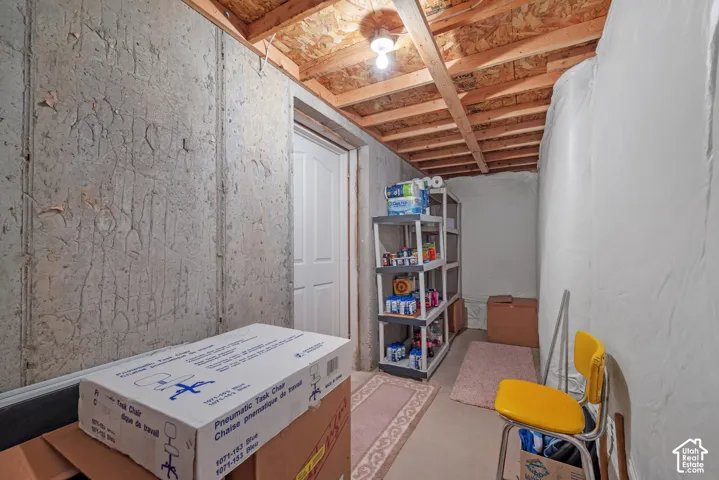 Utility space featuring exposed concrete walls, unpainted wooden ceiling joists, and a white paneled door