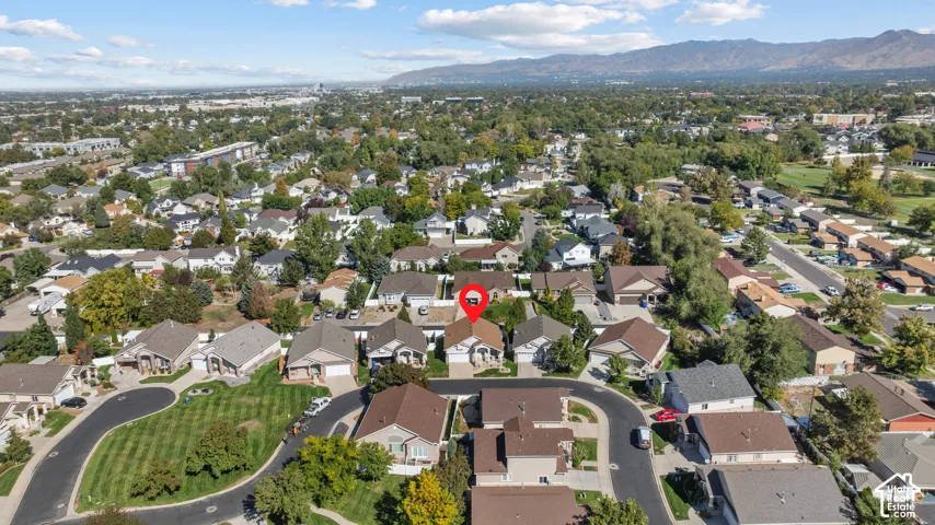 Aerial perspective featuring a single-family residence with a multi-gabled roofline and an attached garage, situated in a residential neighborhood with mountain backdrops