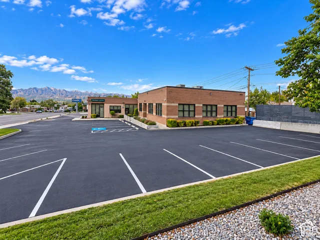 Commercial exterior featuring a brick facade with horizontal banding, expansive asphalt parking lot, and mountain scenery backdrop