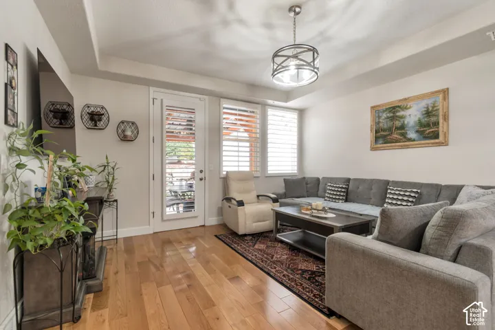 Living area featuring wood-finish flooring, tray ceiling, drum-style pendant lighting, plantation shutters, and a glass-paneled exterior door