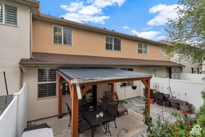 Rear exterior featuring a covered patio with a timber-frame structure, a paved surface, and enclosed white vinyl fencing
