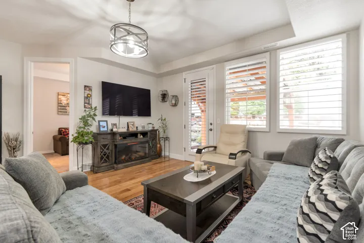 Living area featuring wood-finish flooring, tray ceiling, multi-light drum chandelier, and plantation shutters