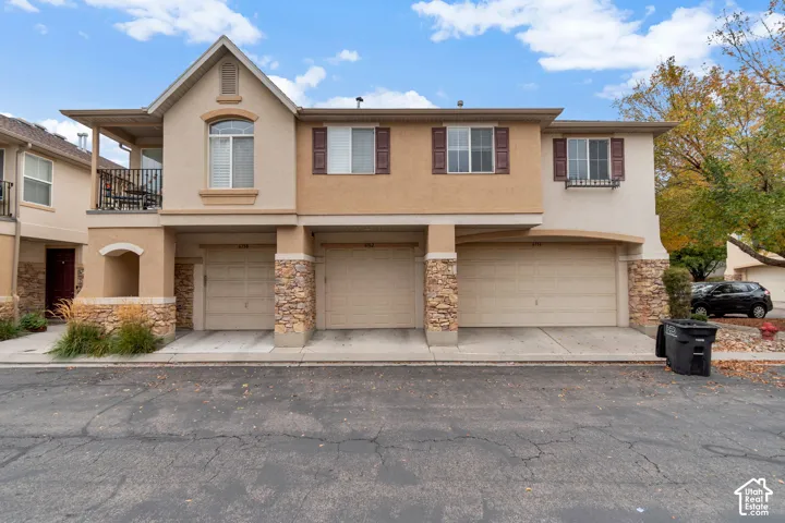 Stucco exterior with stone veneer accents, multi-level design, upper-level balcony with metal railing, and three-bay garage