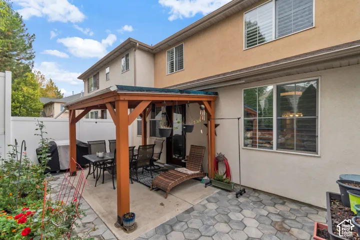 Stucco exterior featuring a wood-frame patio pavilion, hexagonal paver patio, vinyl privacy fencing, and grid-pattern window panes