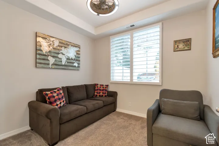Room featuring a recessed tray ceiling, wall-to-wall carpeting, plantation shutters, and a ceiling fan with integrated lighting