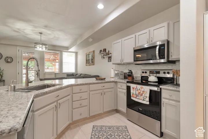 Kitchen featuring light-toned shaker cabinetry, stone-surface countertops, a stainless steel over-the-range microwave, a stainless steel range, and a high-arch kitchen faucet with a pull-down sprayer