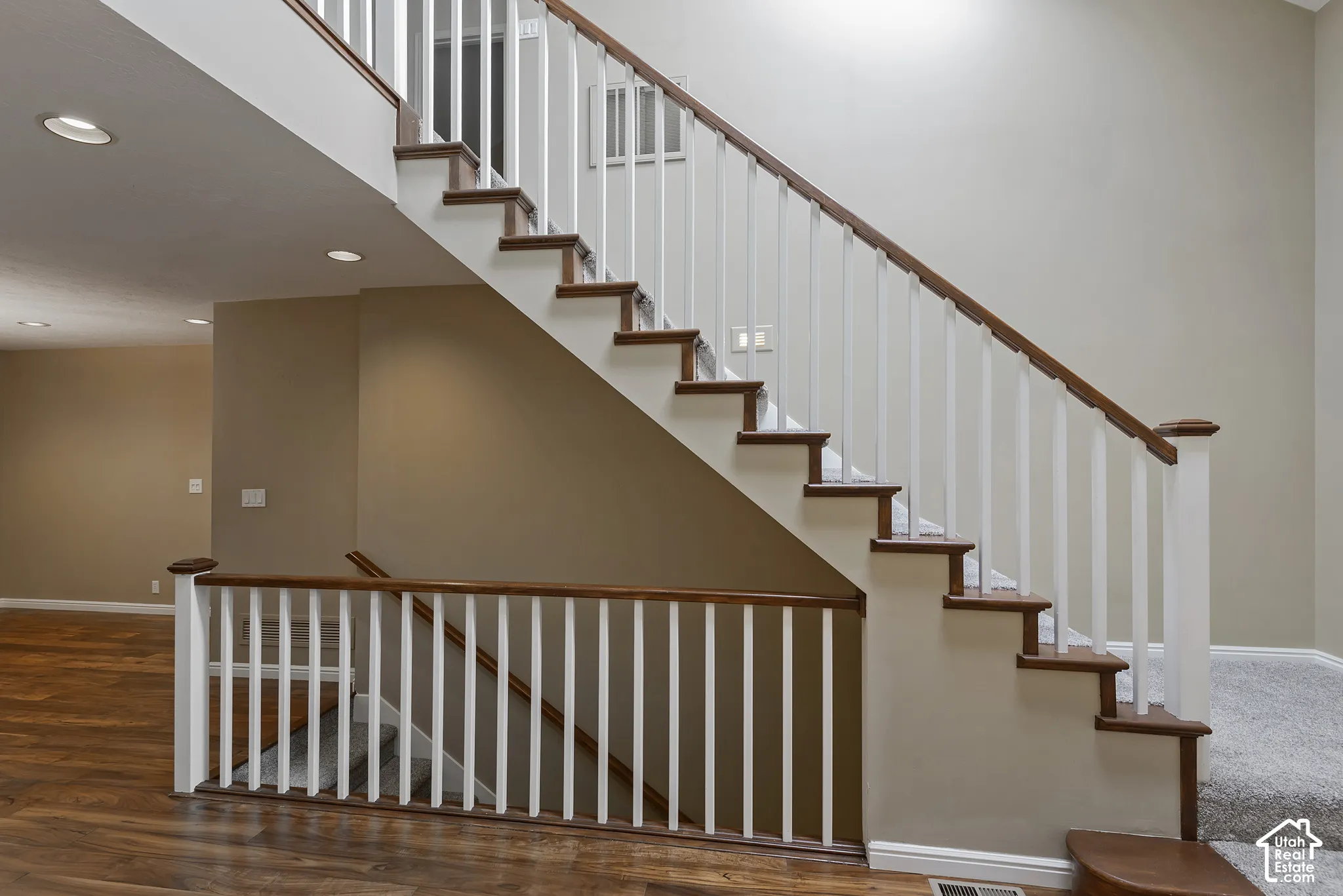 Staircase with wood-finish treads, white balusters, and a rich wood-finish handrail