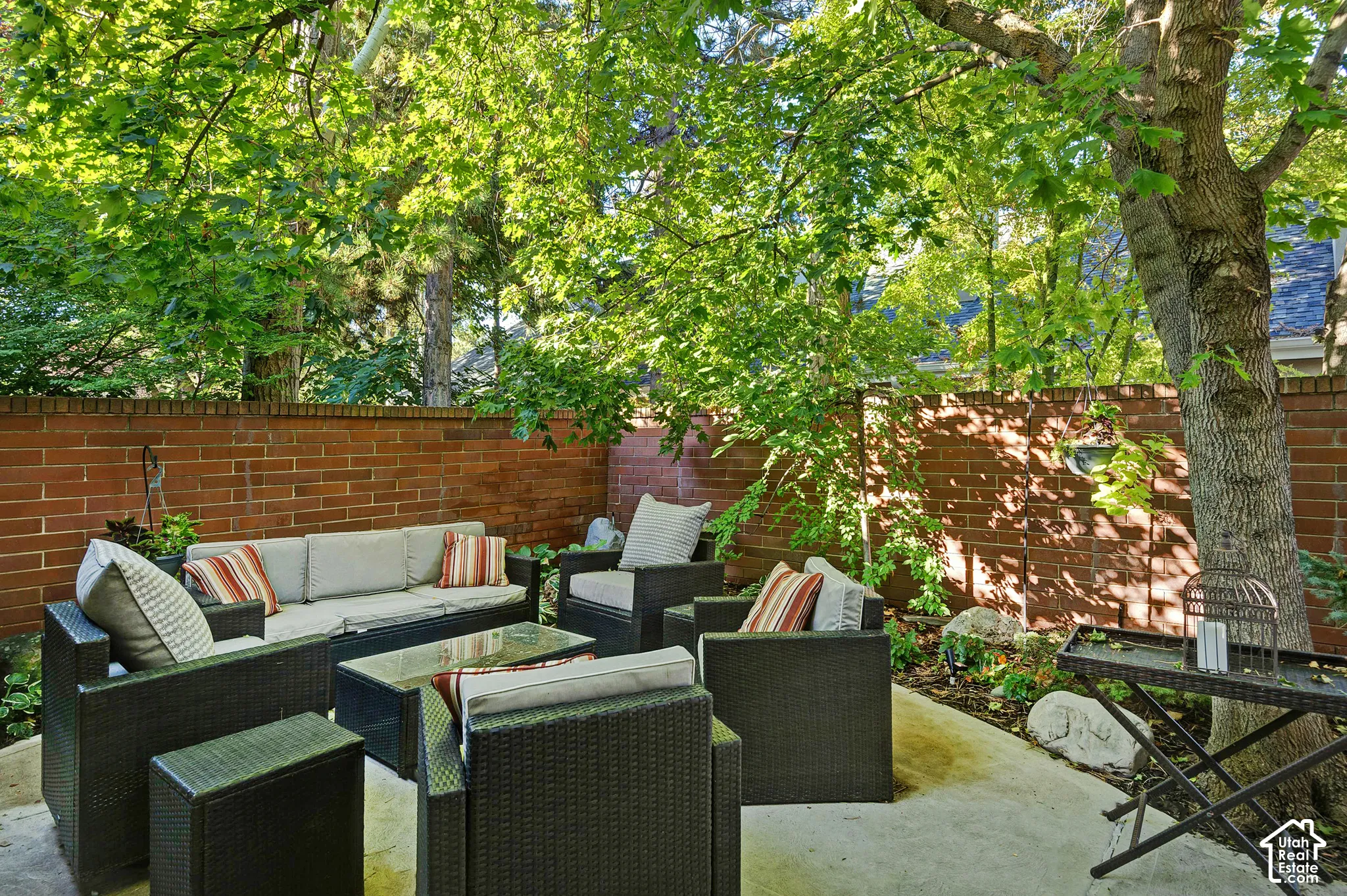 Paved patio area featuring a brick privacy wall and mature trees