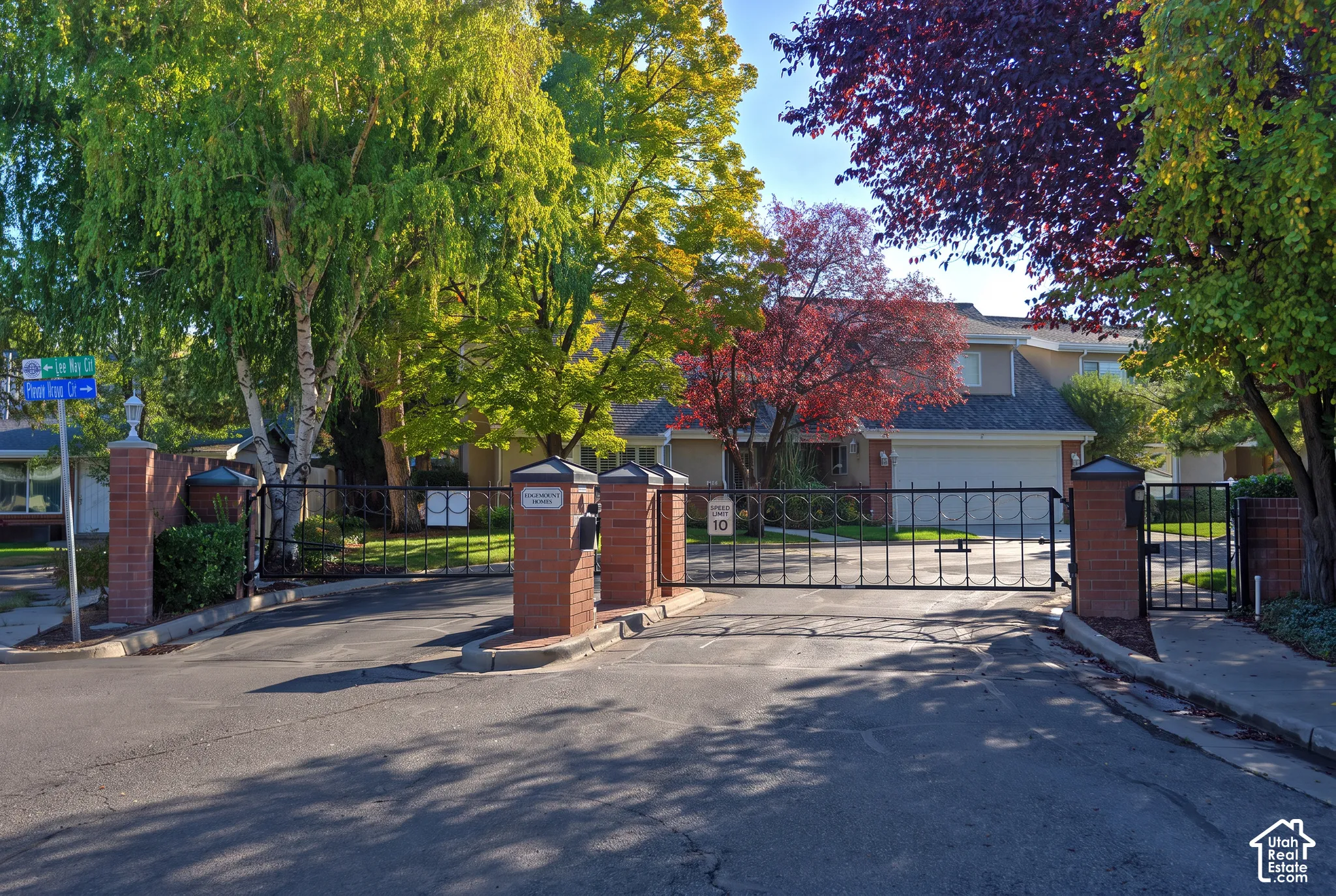 Gated entry featuring brick pillars, wrought iron fencing, and mature trees