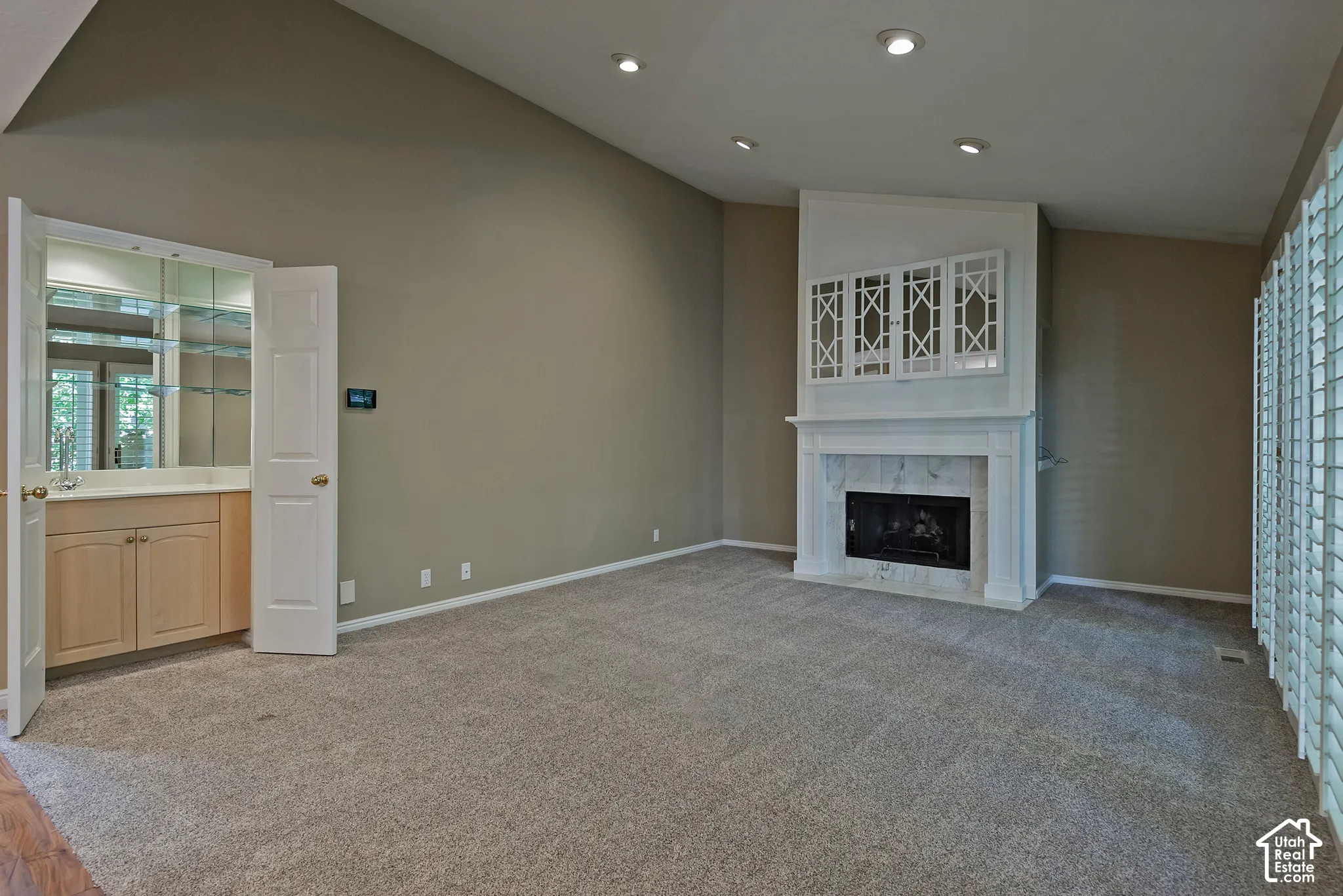 Vaulted ceiling, recessed lighting, built-in wet bar with mirrored backsplash, fireplace with stone surround, and plantation shutters