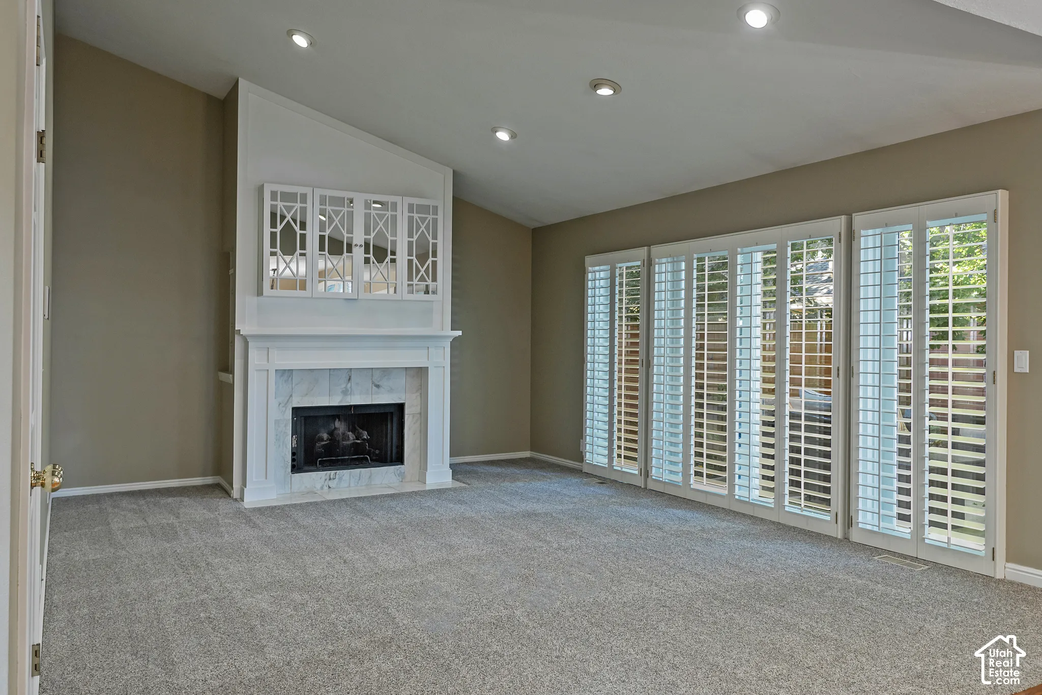 Vaulted ceiling, recessed lighting, fireplace with stone surround, white mantel, and plantation shutters