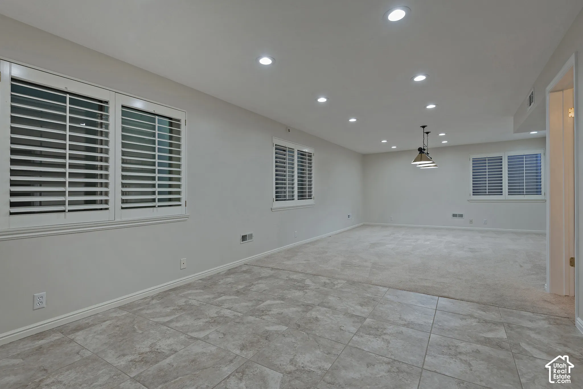 Recessed lighting, plantation shutters, industrial-style pendant fixture, tile flooring, and neutral carpeting