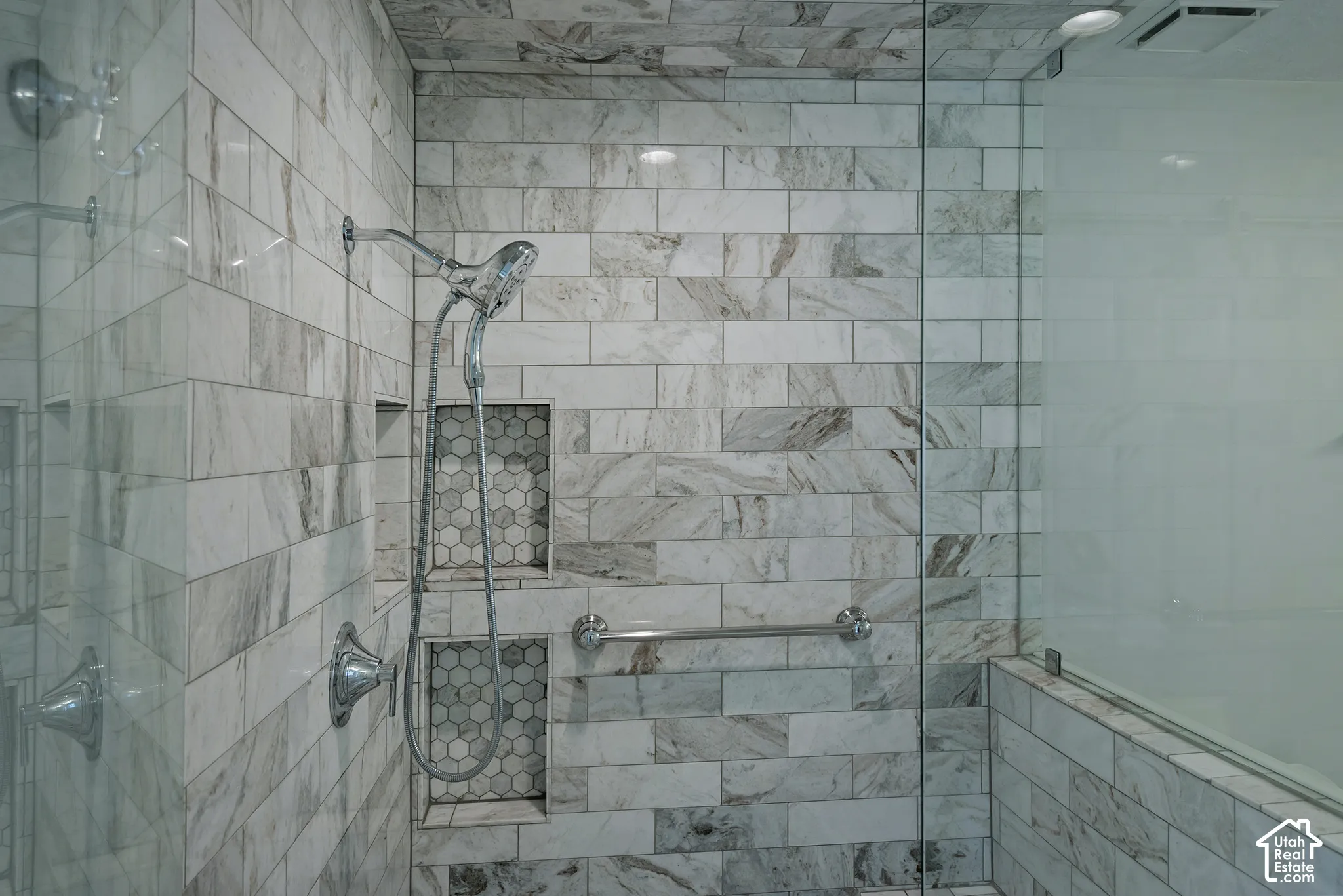 Glass-enclosed shower with subway tile, dual recessed shelves featuring hexagon tile, and a handheld shower fixture