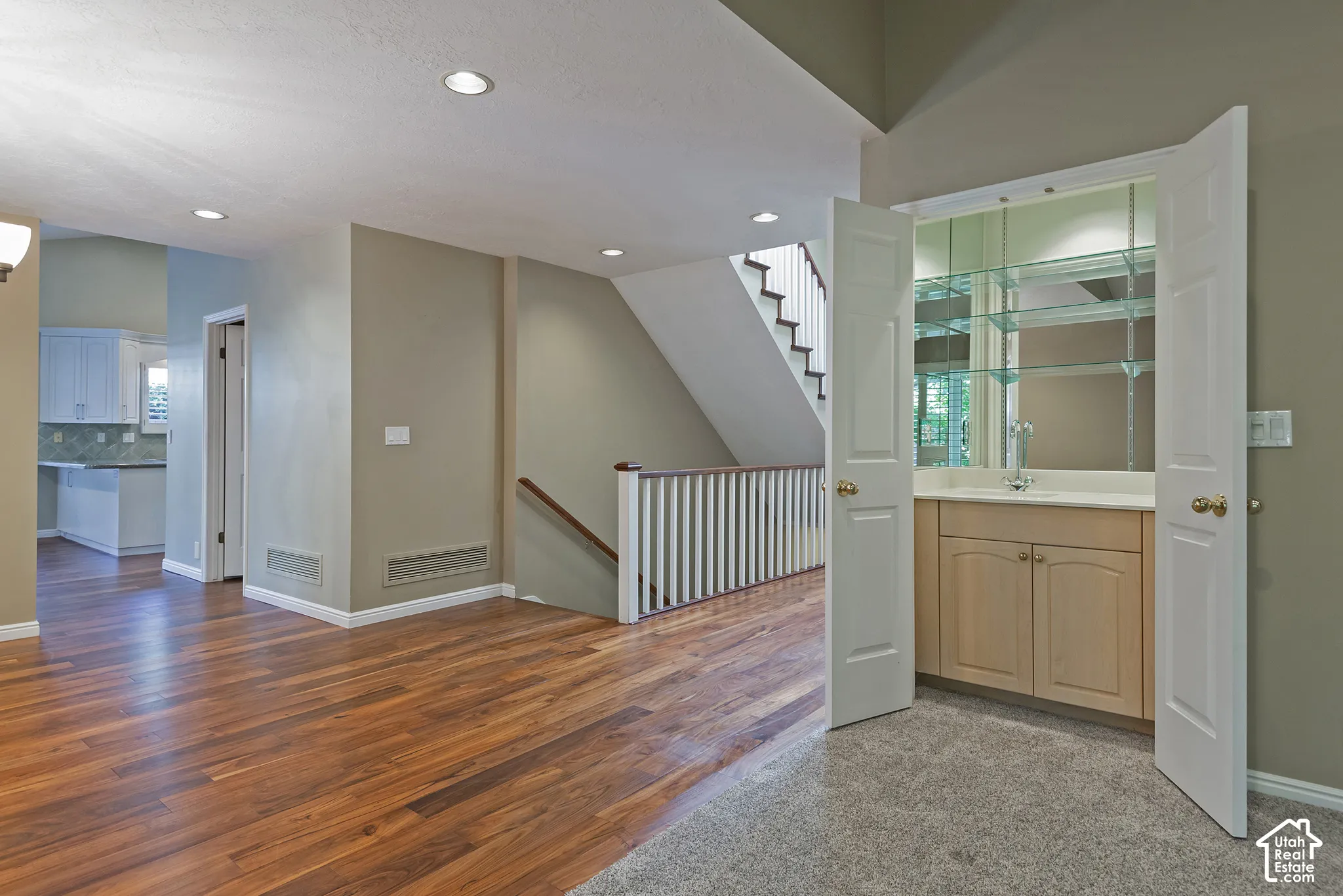 Hardwood-style flooring, a built-in wet bar with mirrored backsplash and glass shelving, recessed lighting, and a staircase with a white balustrade