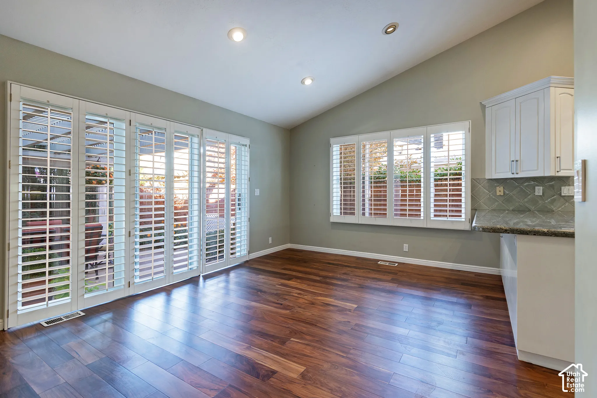 Vaulted ceiling with recessed lighting, wood-finish flooring, plantation shutters, and built-in cabinetry with a stone-finish countertop