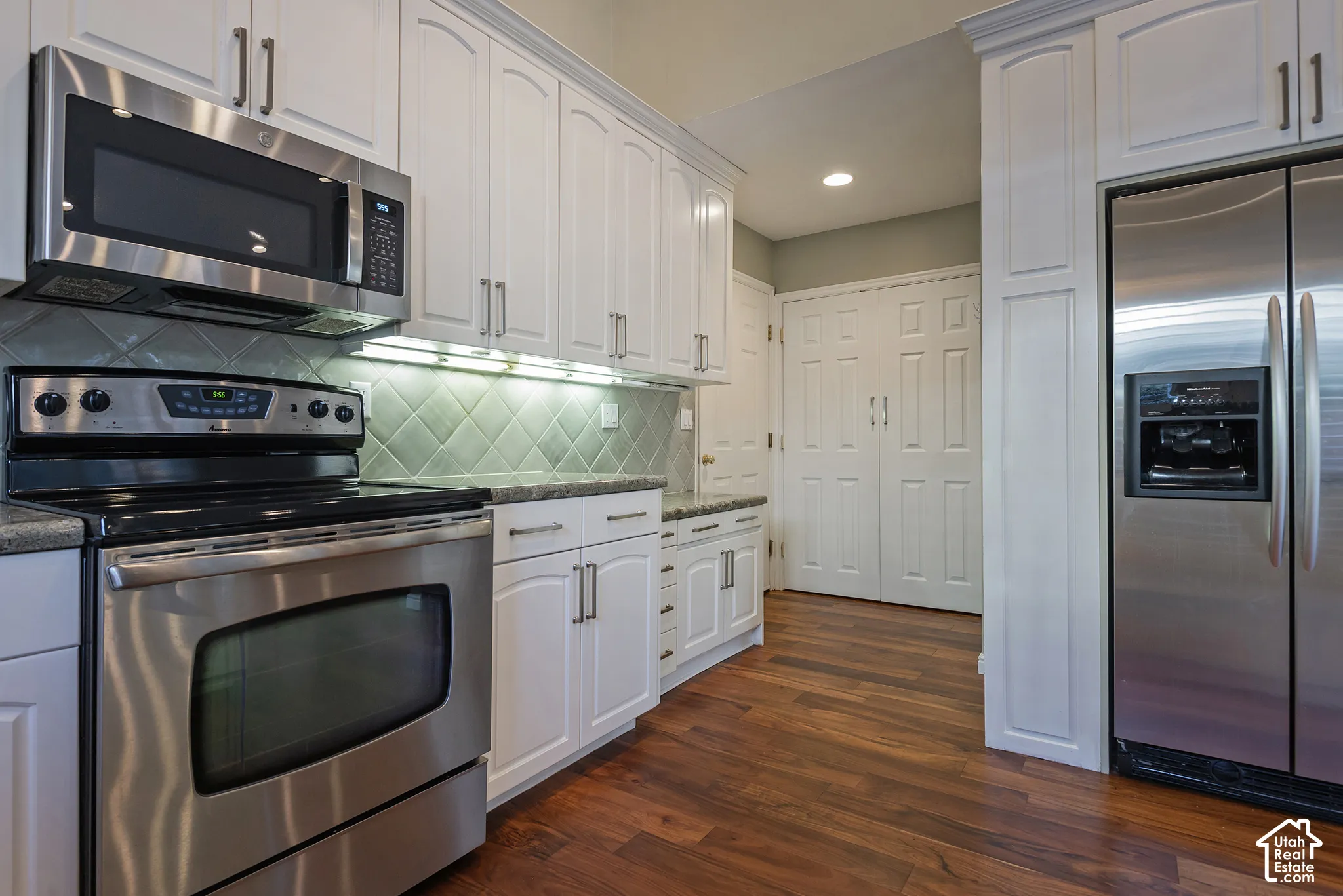 White cabinetry with brushed nickel hardware, stainless steel appliances, speckled countertops, tile backsplash, and wood-finish flooring