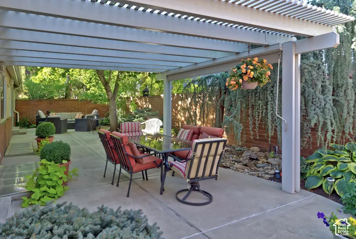 Expansive concrete patio with a slatted pergola, brick privacy wall, and mature landscaping