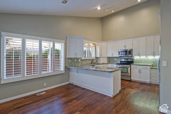 High ceilings, white shaker cabinetry, stainless steel appliances, granite countertops, and wood-finish flooring