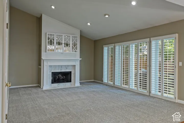 Vaulted ceiling, recessed lighting, fireplace with stone surround, white mantel, and plantation shutters