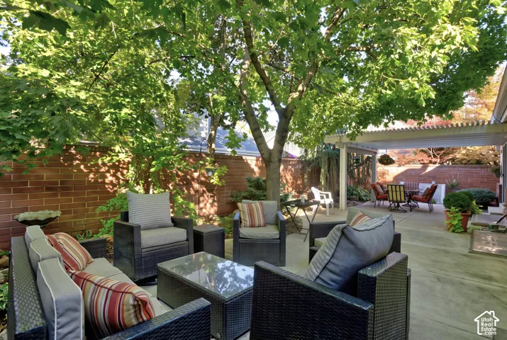 Expansive concrete patio featuring a large mature tree, a red brick privacy wall, and a white pergola structure