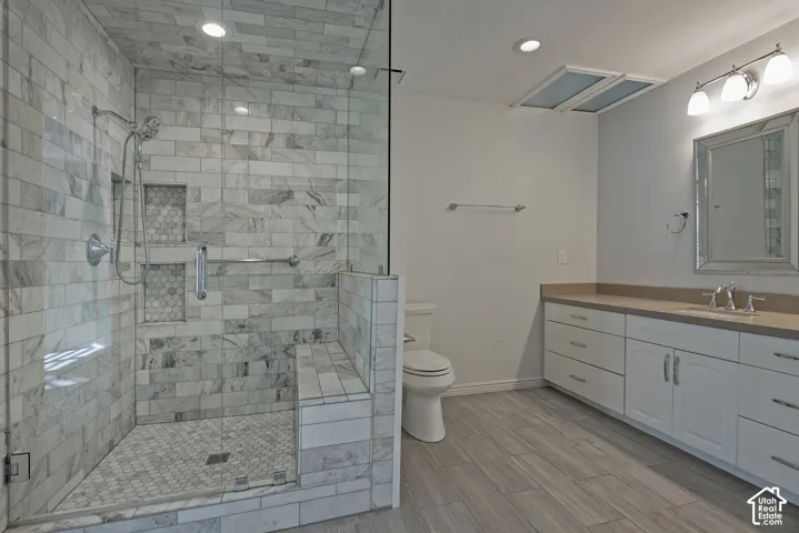Glass-enclosed shower with subway tile and built-in bench, dual recessed shower niches, wood-finish flooring, an extended vanity with dual sinks, and white cabinetry