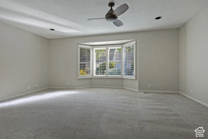Spacious room featuring a bay window with white plantation shutters, neutral carpet, recessed lighting, and a ceiling fan
