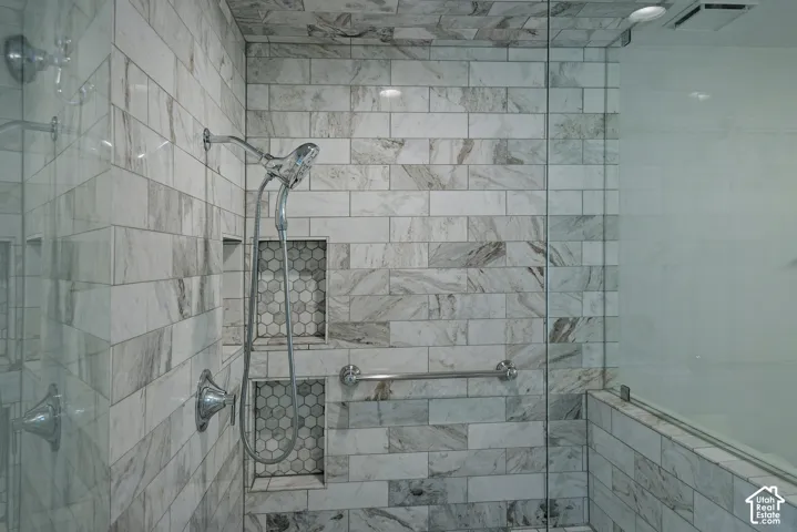 Glass-enclosed shower with subway tile, dual recessed shelves featuring hexagon tile, and a handheld shower fixture