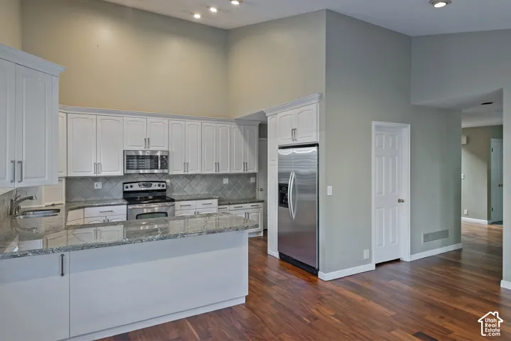 Kitchen with vaulted ceiling, white cabinetry, stainless steel appliances, and wood-finish flooring