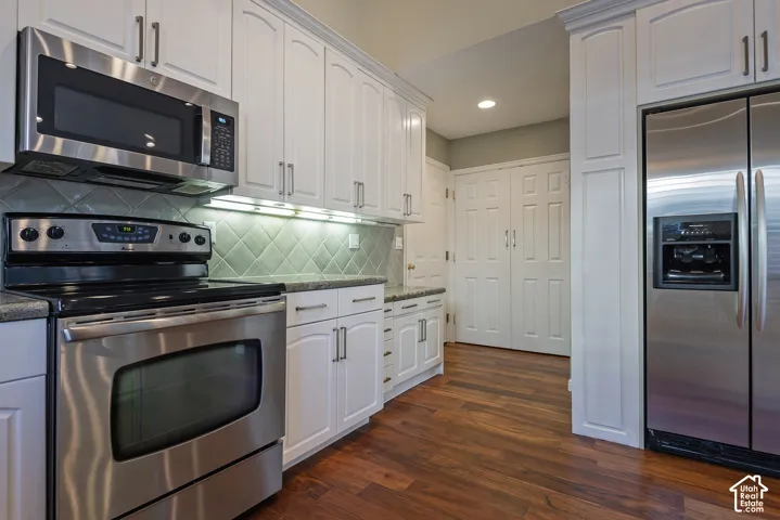 White cabinetry with brushed nickel hardware, stainless steel appliances, speckled countertops, tile backsplash, and wood-finish flooring
